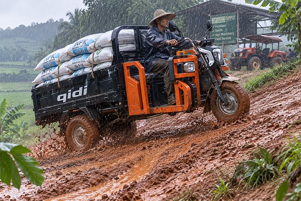 QIDI electric tricycle navigating muddy village road during monsoon season in Southeast Asia